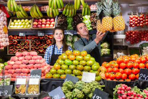 Male and female shop assistants laying out fruits and vegetables behind the counter photo