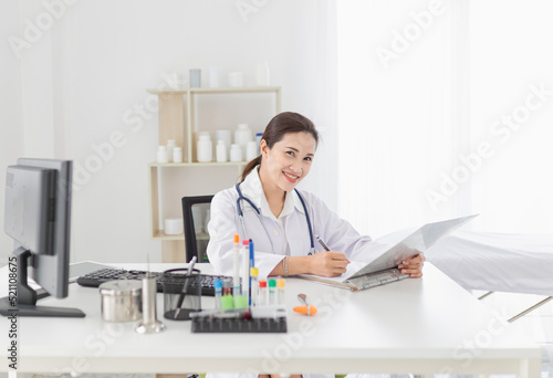 asian female doctor reading and order treatment process on patient chart, she sitting and smile in hospital