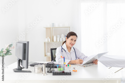 asian female doctor reading and order treatment process on patient chart, she sitting and smile in hospital