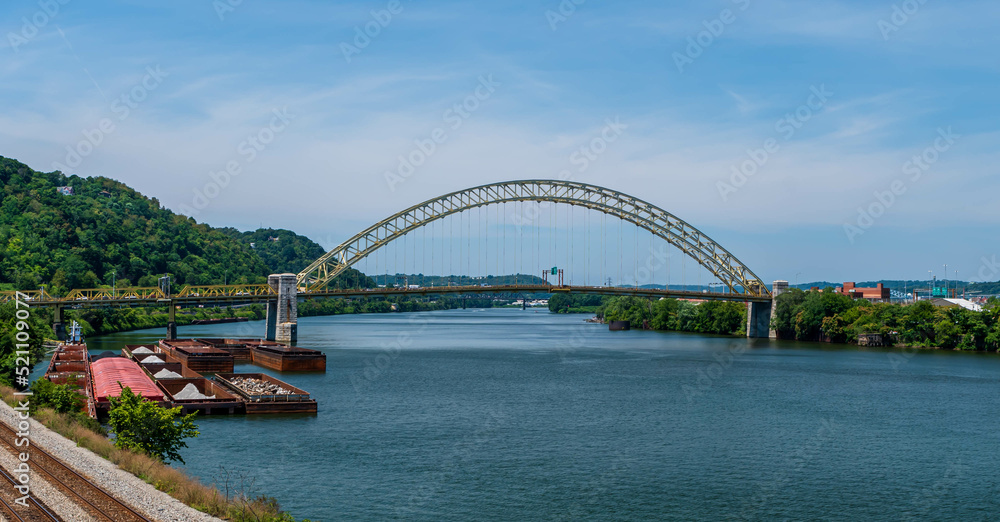 The West End Bridge that spans the Ohio River and connects the north side and the west end in Pittsburgh, Pennsylvania, USA. Several barges and a tugboat are moored to the west end shoreline
