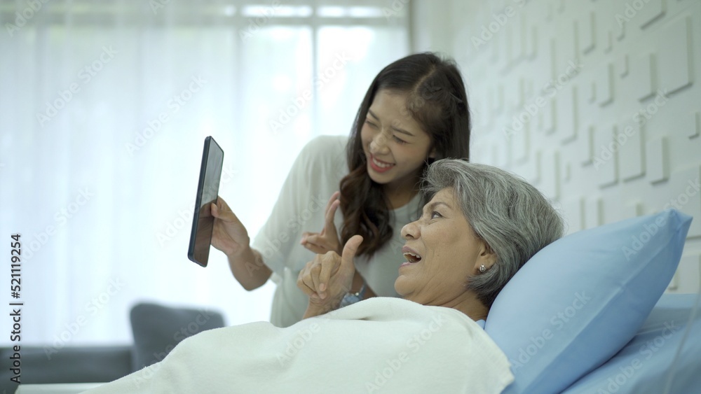 Senior elder Asian female patient resting on the medical bed in hospital and talking to her daughter. daughter visiting  his mother in hospital and let her talk to family on a video call.