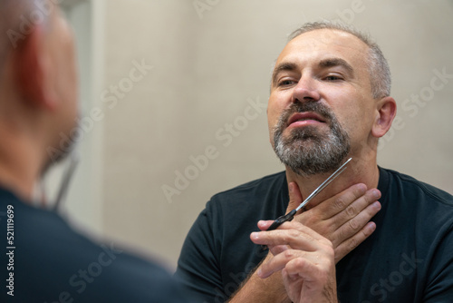 Middle-aged handsome man using scissors to cut his beard a litlie and fix the shape photo