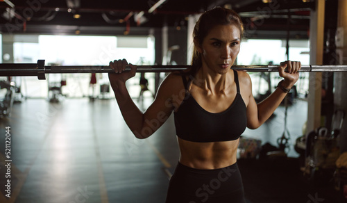 Sporty woman exercising with barbell in fitness class. Workout woman in gym with barbell.