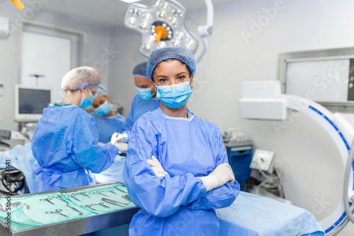 Portrait of female woman nurse surgeon OR staff member dressed in surgical scrubs gown mask and hair net in hospital operating room theater making eye contact smiling pleased happy looking at camera photo