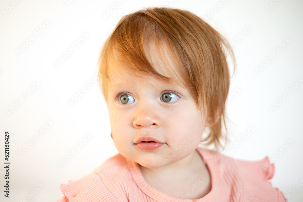 Portrait of a charming funny red-haired baby girl with blue eyes and a birthmark on her cheek. Hemangioma. Light background. Lifestyle Portrait of a charming funny red-haired baby girl with blue eyes and a birthmark on her cheek. Hemangioma. Light background. Lifestyle