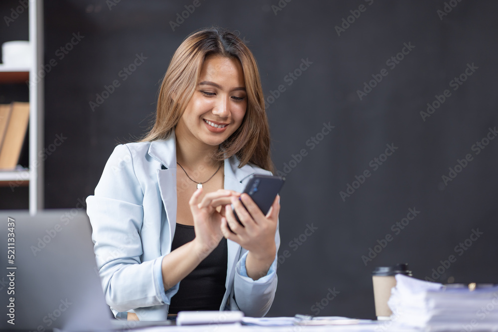 Asian women hold smartphone and use pc at the workplace. Project stats financial data sales charts on laptop and cellphone Asian women hold smartphone and use pc at the workplace. Project stats financial data sales charts on laptop and cellphone