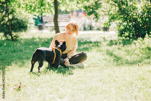 Black french Bulldog Puppy cuddling up with owner girl laying on lawn in park outdoors summer spring day kissing hugging petting. Happy woman with dog outside © Olga Krivokoneva