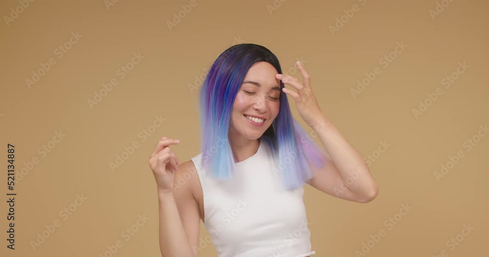 Young Asian woman in color wig enjoys dancing in beige studio Young Asian woman in color wig enjoys dancing in beige studio