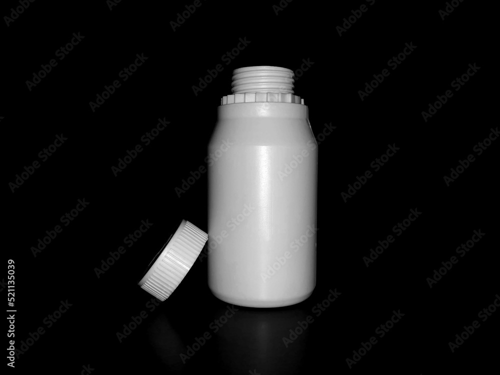 The empty plastic white bottle is on a dark background. The empty plastic white bottle is on a dark background.