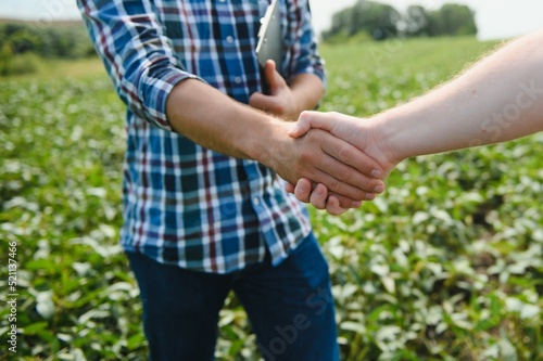 Two farmers shaking hands in soybean field in early summer © Serhii