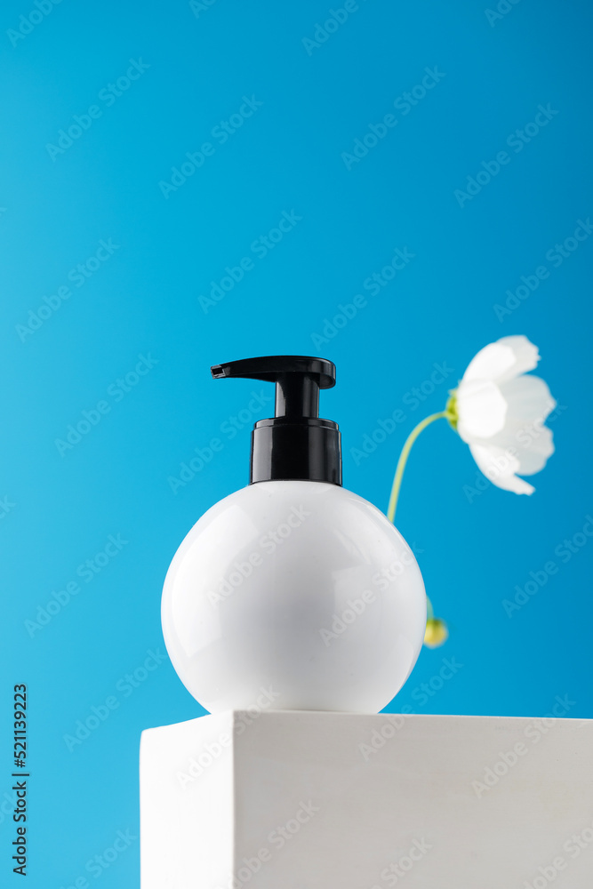 Obraz premium Mockup of a white dispenser with a cosmetic product with a place for your logo on a podium on a blue background.