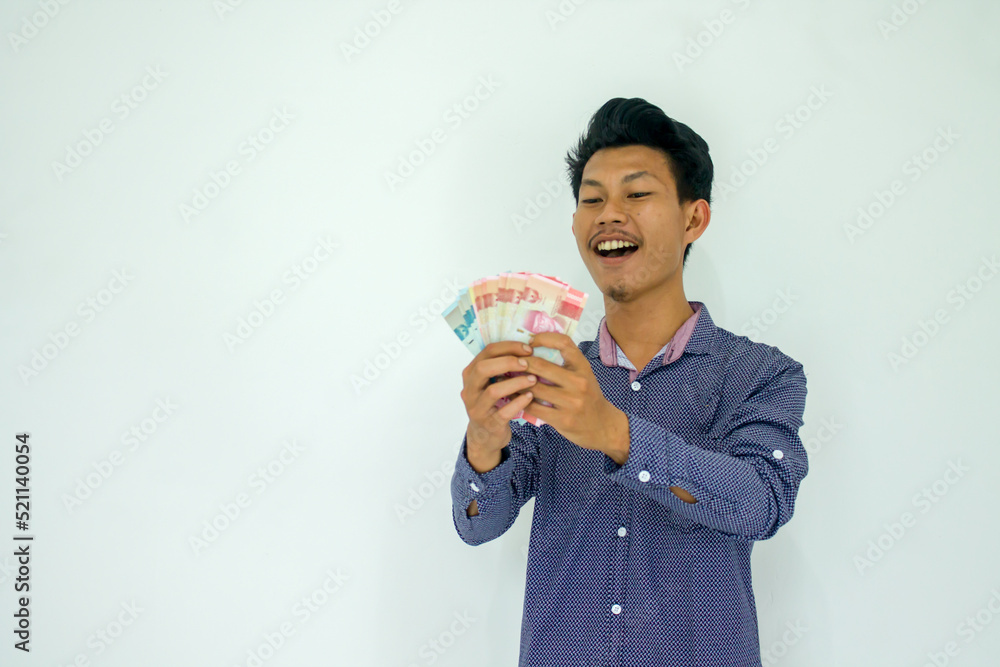 Portrait of happy young Indonesian man holding rupiah money isolated on white background with copy space. Portrait of happy young Indonesian man holding rupiah money isolated on white background with copy space.