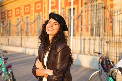 Young, beautiful woman with dark, curly hair gesturing to the camera. She is sightseeing in front of a monument and you can see a bicycle in the background. Holiday and tourism concept.