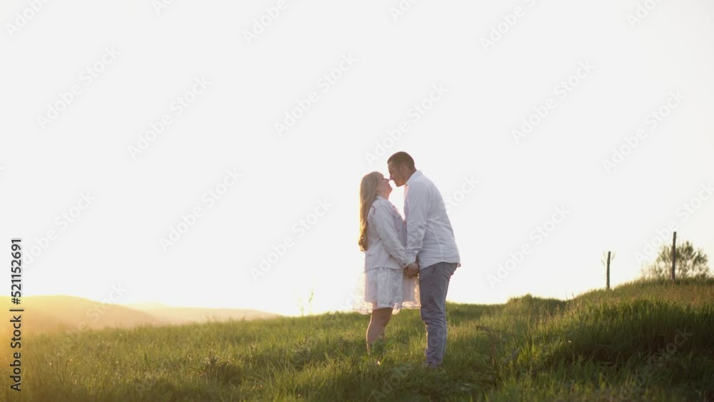 Happy couple having fun against the background of the sunset in the field. A guy and a girl in love are walking, hugging, resting in nature in the summer. Holding hands, looking at the bright sunset. Happy couple having fun against the background of the sunset in the field. A guy and a girl in love are walking, hugging, resting in nature in the summer. Holding hands, looking at the bright sunset.