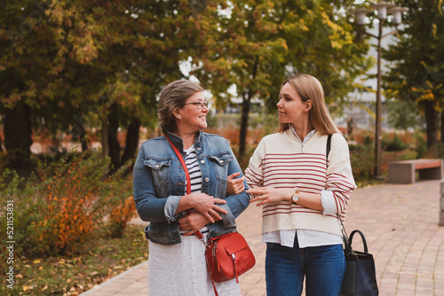 middle aged blond mother and adult daughter walks and having fun in autumn park
