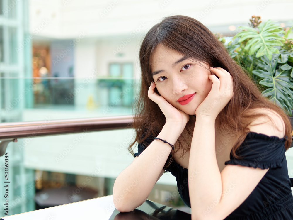 Portrait of beautiful Chinese young girl wearing black tube dress sitting and smiling at camera in shopping mall, indoor fashion portrait of glamour sexy stylish lady with black long hair. Portrait of beautiful Chinese young girl wearing black tube dress sitting and smiling at camera in shopping mall, indoor fashion portrait of glamour sexy stylish lady with black long hair.