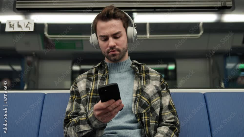 Focused young man rides the subway, listens to music with wireless headphones and uses a