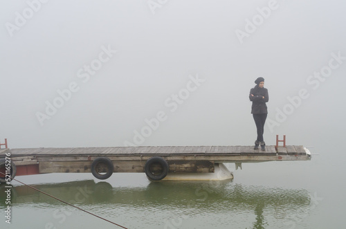 Young woman standing on the river dock surrounded by winter mist