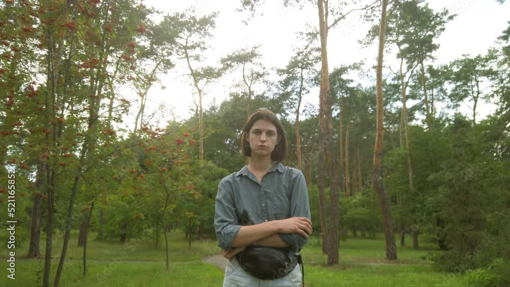 Portrait of young depressed woman standing at the park looking into the camera. Female with sad mood Portrait of young depressed woman standing at the park looking into the camera. Female with sad mood