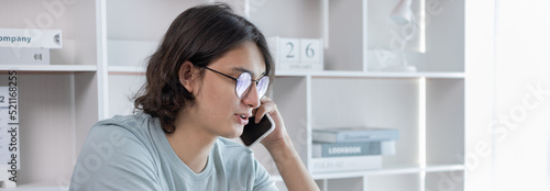 Asian man talking on the phone and working on a laptop with a smiling face, Business Cell Phone Conversations, Working at home, Home lifestyle, Stay home, New normal, learning, Social distancing.