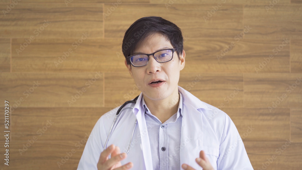 A portrait of Asian doctor man smiling, talking to a patient on video call conference online in hospital or clinic with medical gown cloth uniform in medical, healthcare. People lifestyle. A portrait of Asian doctor man smiling, talking to a patient on video call conference online in hospital or clinic with medical gown cloth uniform in medical, healthcare. People lifestyle.