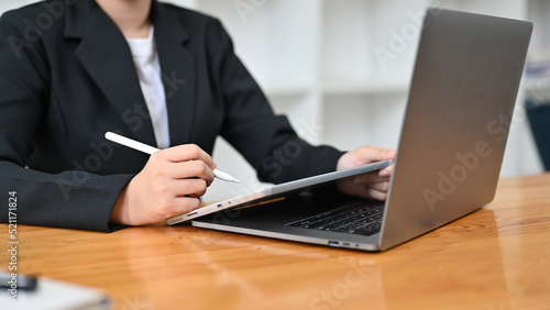 Cropped, Professional asian businesswoman sits at her office desk, using tablet and computer.
