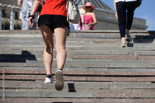Woman wearing short black shorts going up the stone stair on people background. Female fashion and footwear in summer city