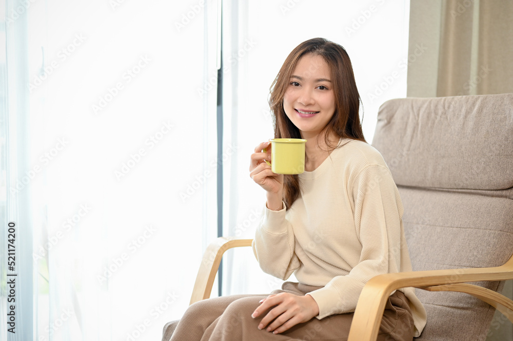 Relaxed and beautiful young Asian woman is on her armchair while having a coffee.