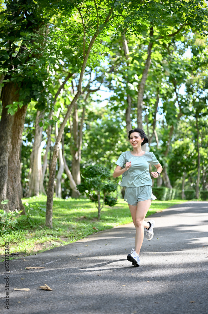 Portrait, Healthy fit millennial Asian woman running or jogging in the green city park.