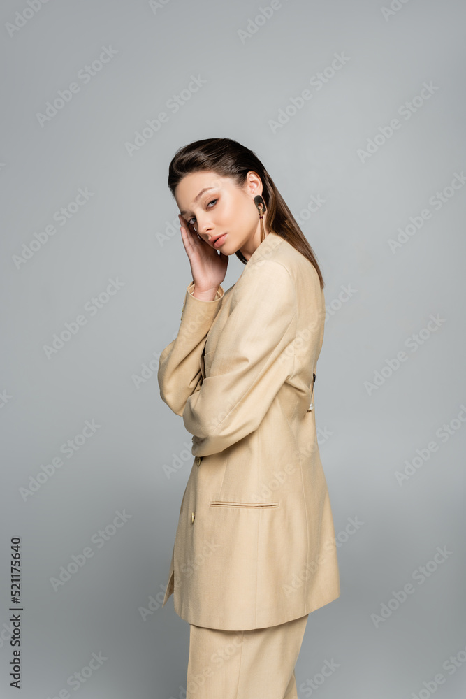 brunette model in beige blazer looking at camera while posing isolated on grey brunette model in beige blazer looking at camera while posing isolated on grey
