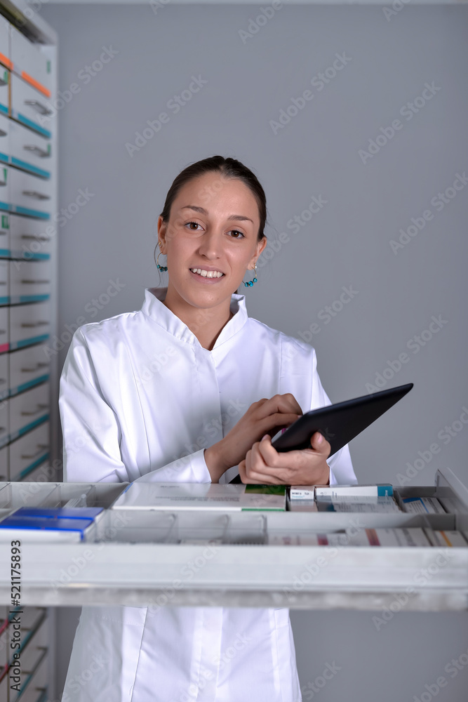 A Young pharmacist standing next to medicine shelves, holding tablet A Young pharmacist standing next to medicine shelves, holding tablet