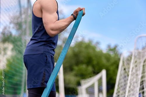 Strong athlete swings his biceps with a sports band in the stadium. Training process on the hands of a muscular athlete in the fresh air