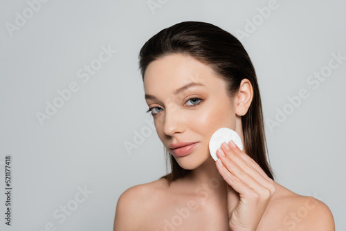 young woman removing makeup with soft cotton pad isolated on grey