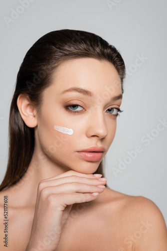 young woman with bare shoulders and cream on face looking at camera isolated on grey