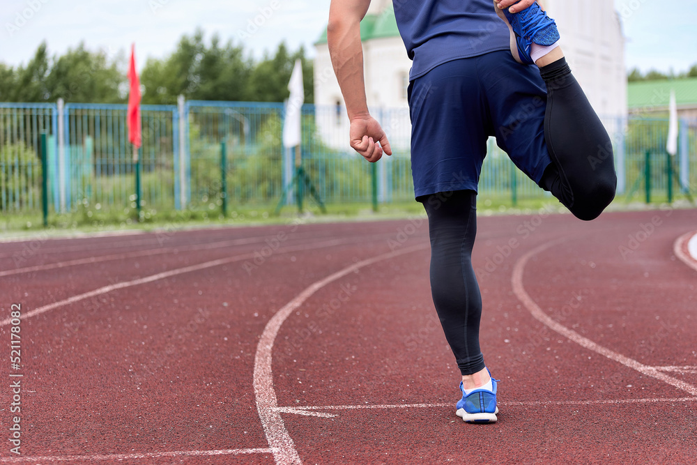Obraz premium Runner kneads his legs in stadium before race on a circular treadmill with a rubber coating. Long-legged athlete in a sports uniform prepares for the starting race, kneads the muscles of the legs