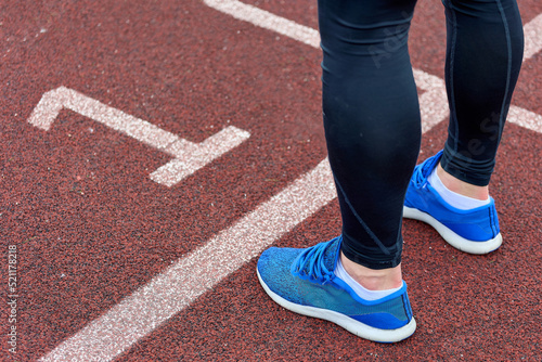 An athlete runner trains in the stadium, standing at the white line on track number one. Close-up of the leg of a runner in blue sneakers before the marathon race on the first track