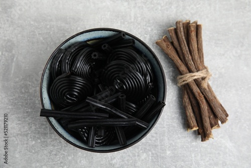 Tasty black candies and dried sticks of liquorice root on grey table, flat lay photo
