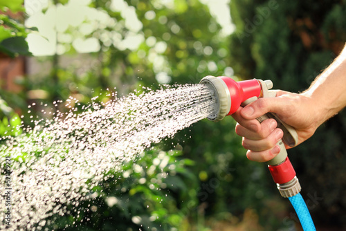 Man spraying water from hose in garden, closeup photo