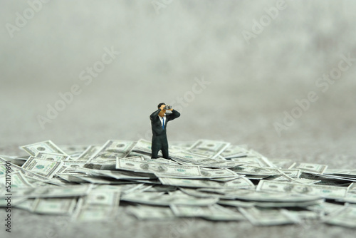 Miniature people figure toys photography. Inflation and recession concept. Businessmen standing above dollar money pile using binoculars searching for solution