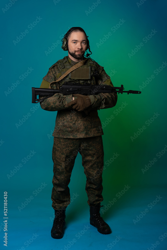 soldier in the studio on a green background with colored light. a man in military uniform with a gun, rifle or machine gun. military. airball player soldier in the studio on a green background with colored light. a man in military uniform with a gun, rifle or machine gun. military. airball player
