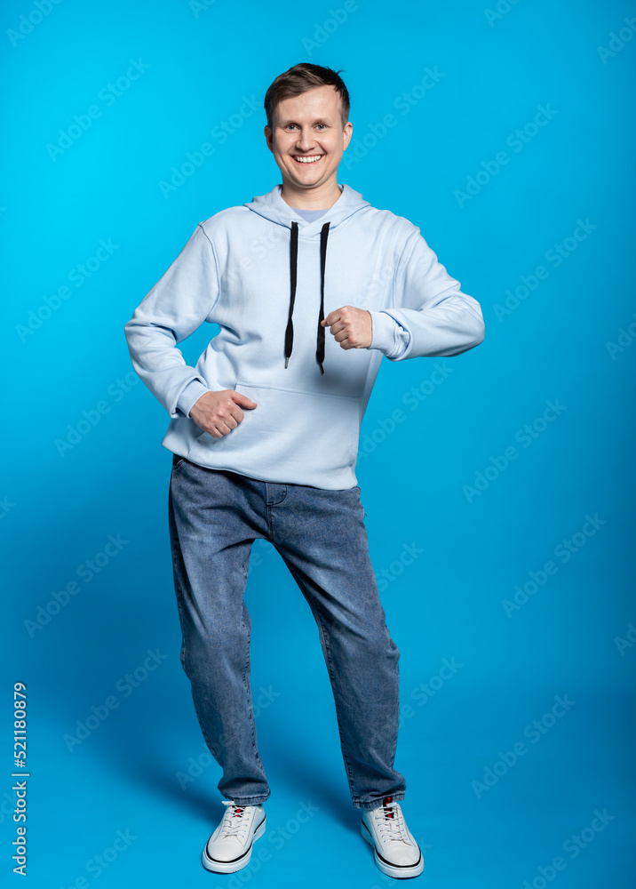a guy in a blue sweatshirt and jeans is dancing. full height. blue background a guy in a blue sweatshirt and jeans is dancing. full height. blue background