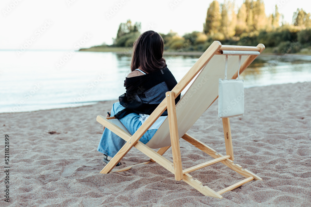 Girl sitting in the deckchair on the beach looking at water