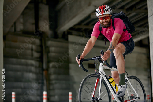 Portrait of a cyclist standing under a bridge with a bicycle in his hand, posing at the camera against an architecture background. Active lifestyle. Cycling is a hobby.