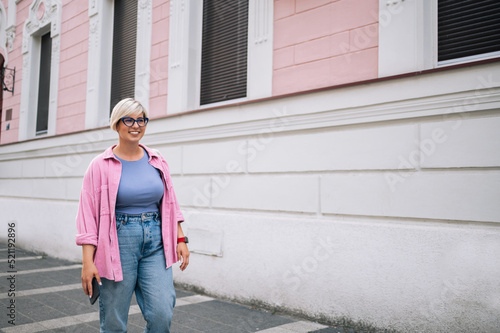 Plus size woman with pixie hair using smartphone in the city street.