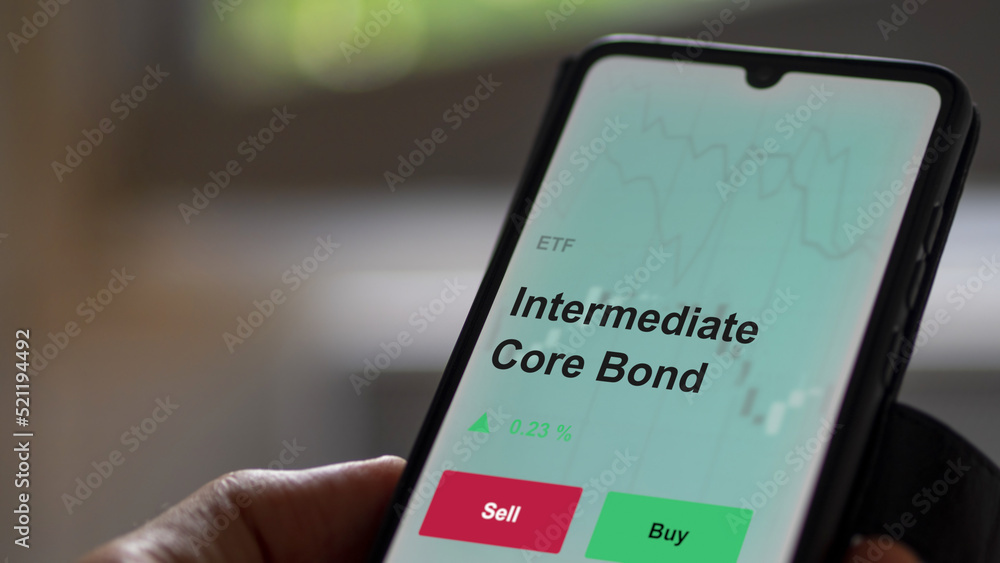An investor's analyzing the intermediate core bond etf fund on a screen. A phone shows the prices intermediate-term An investor's analyzing the intermediate core bond etf fund on a screen. A phone shows the prices intermediate-term
