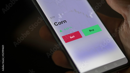 An investor's analyzing the corn etf fund on a screen. A phone shows the prices of cereal traded ETF.