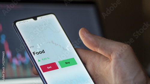 An investor's analyzing the food etf fund on a screen. A phone shows the prices of Food
