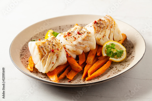 Fried pieces of cod loin, served with sweet potato fries. Light stone background.