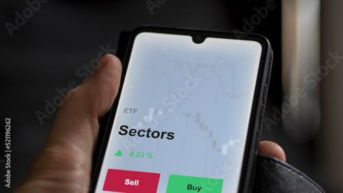 An investor's analyzing the sectors etf fund on a screen. A phone shows the prices of an ETF to invest in blue chips.