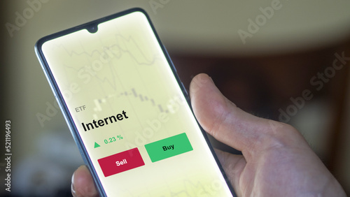 An investor's analyzing the internet etf fund on a screen to invest. A phone shows the prices of web ETF blue chips.. 